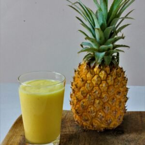 Refreshing glass of pineapple juice beside a ripe pineapple on a wooden table.