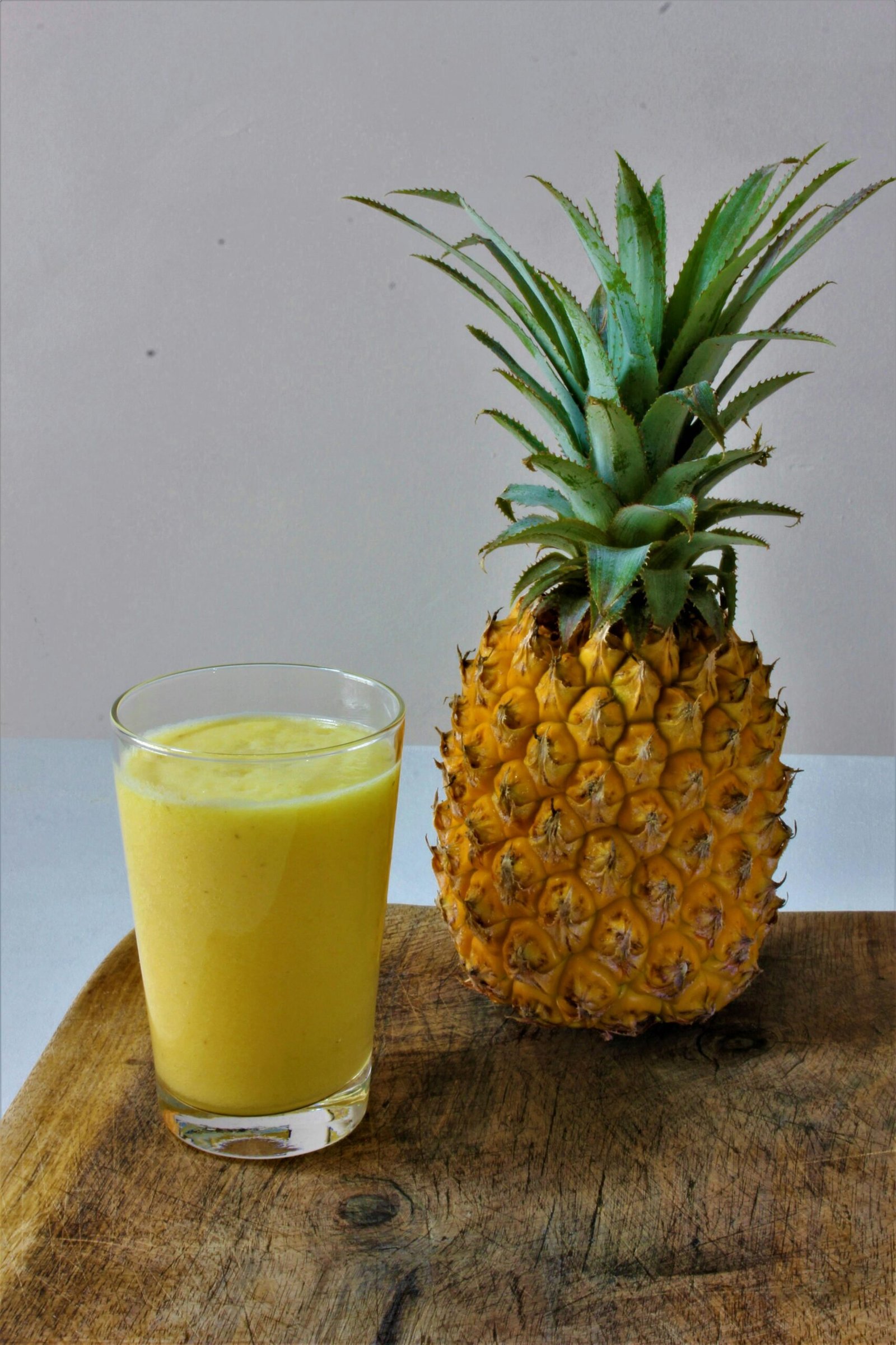Refreshing glass of pineapple juice beside a ripe pineapple on a wooden table.